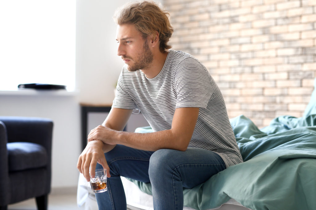 Depressed young man drinking alcohol at home
