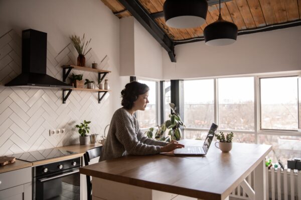 A woman sitting in her kitchen working on her laptop from the kitchen island.